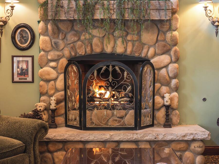 A stone fireplace with a fire, surrounded by a stone wall, with framed pictures and a bear statue on the mantel.
