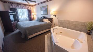 A hotel room with a bed, a bathroom with a bathtub, a ceiling fan, and a window with curtains.