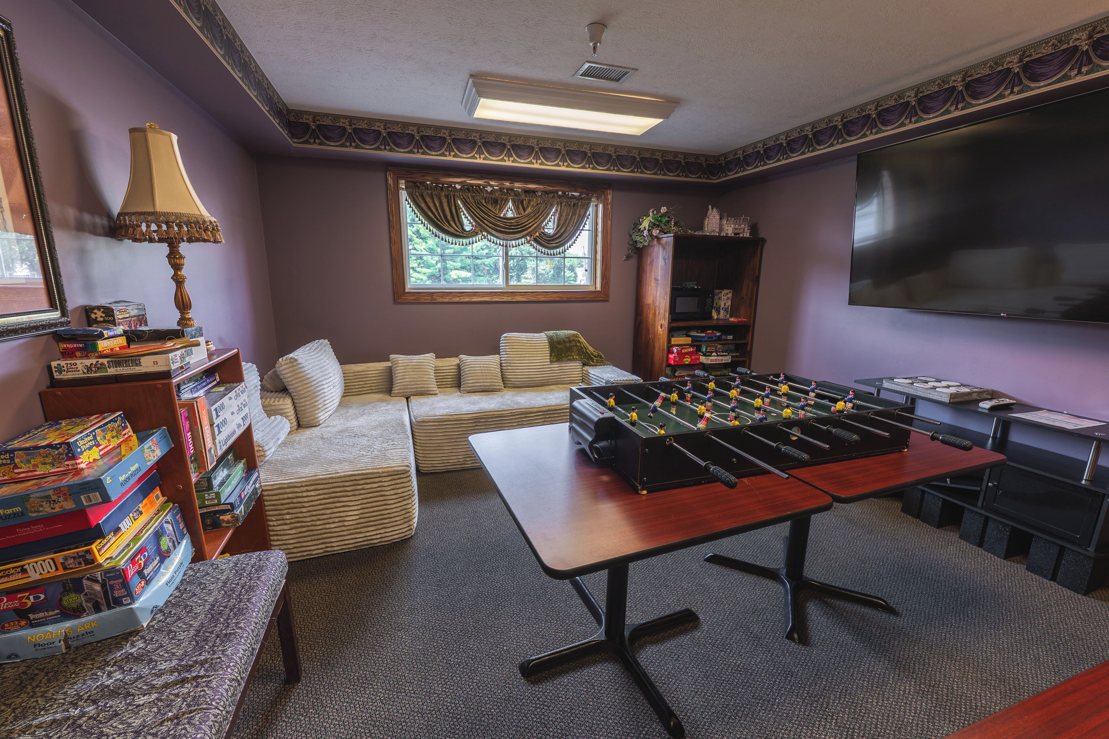 Una habitación con mesa de futbolín, sofá, estantería y televisor.