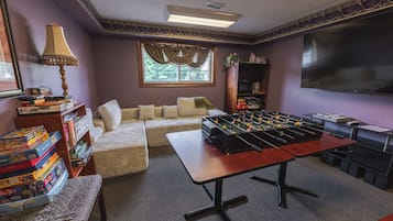 Una habitación con mesa de futbolín, sofá, estantería y televisor.