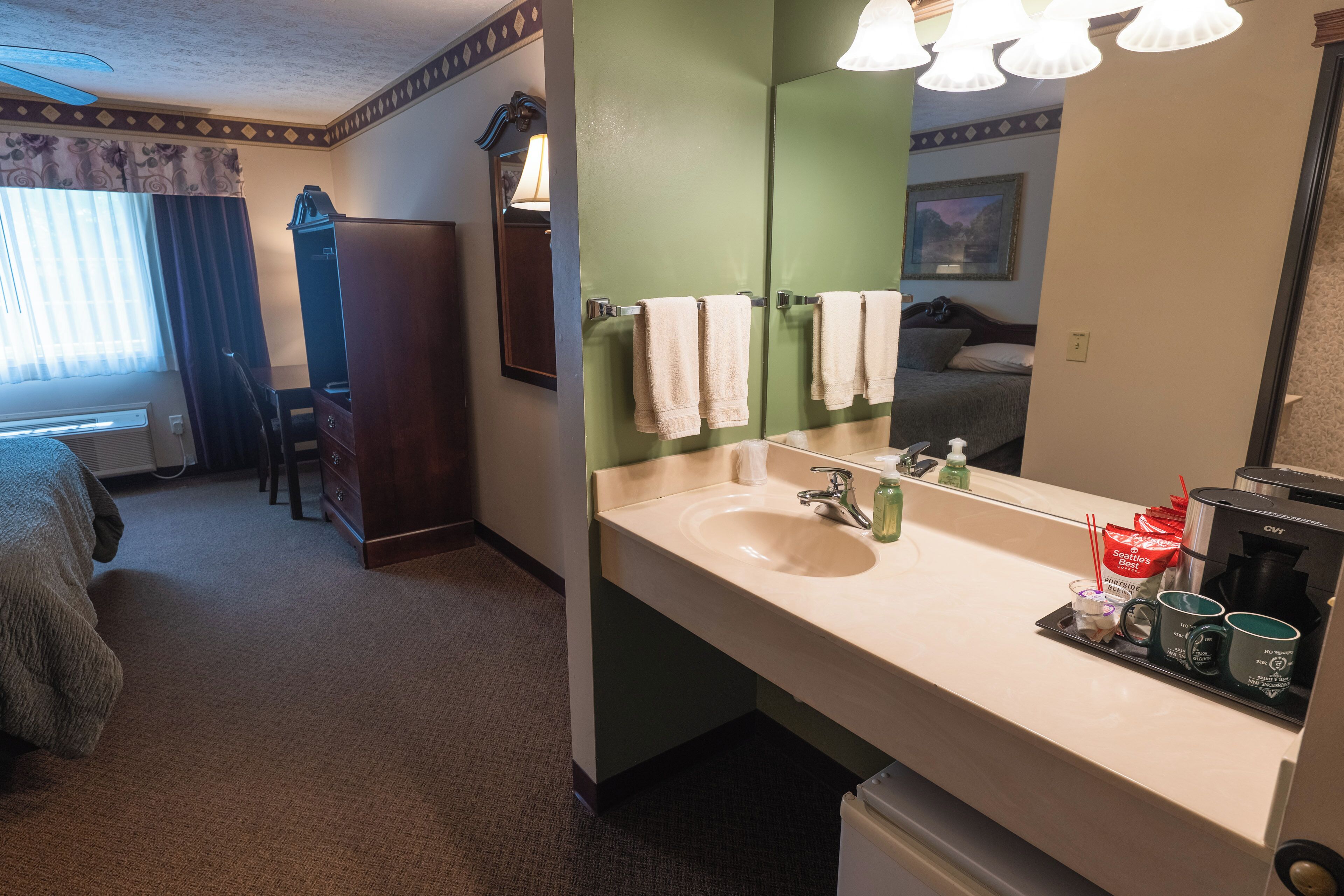 A hotel room with a large mirror, a sink, a coffee maker, and a bed.