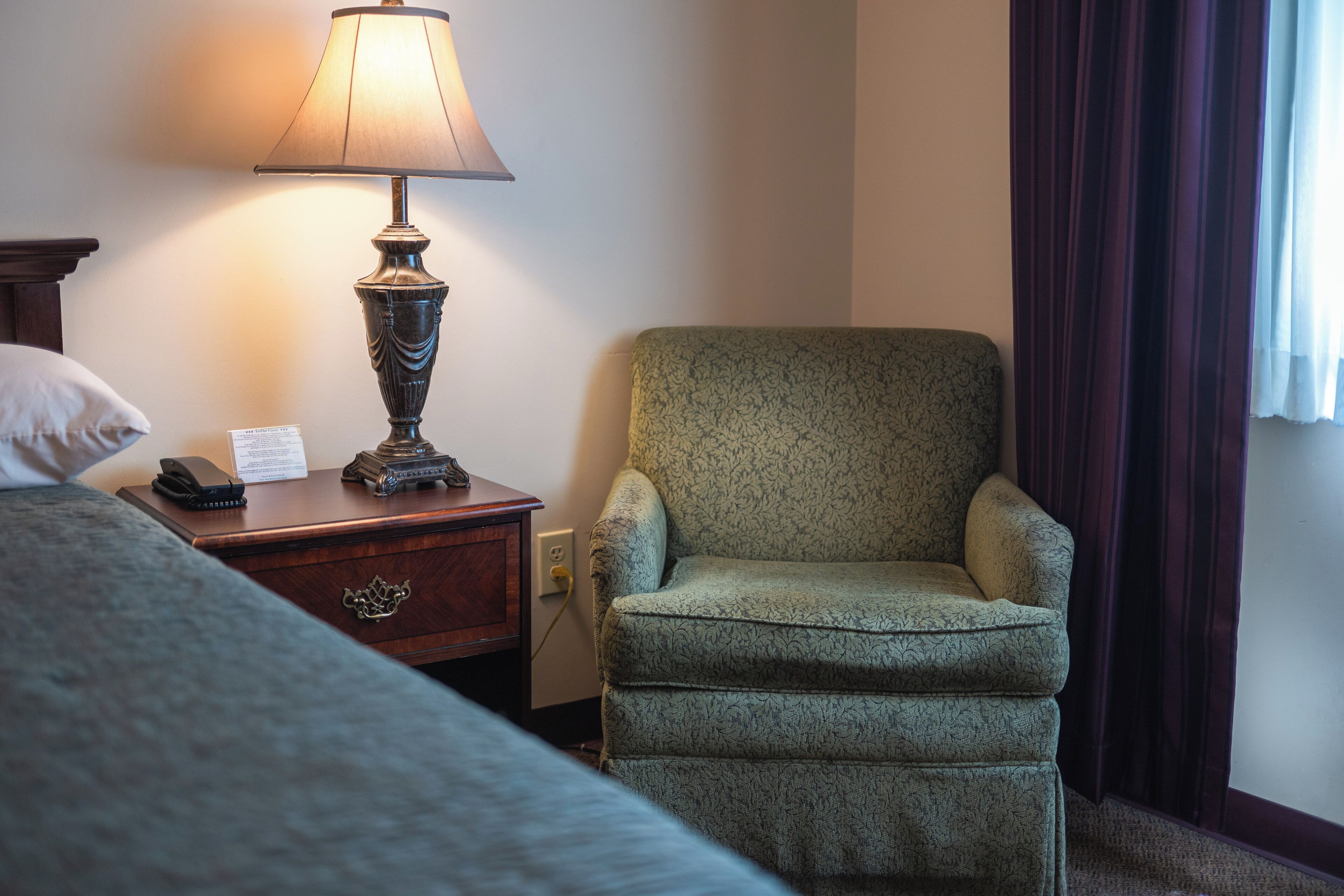 Una habitación de hotel con cama, una silla, una lámpara y una mesita de noche.
