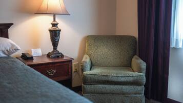 Una habitación de hotel con cama, una silla, una lámpara y una mesita de noche.