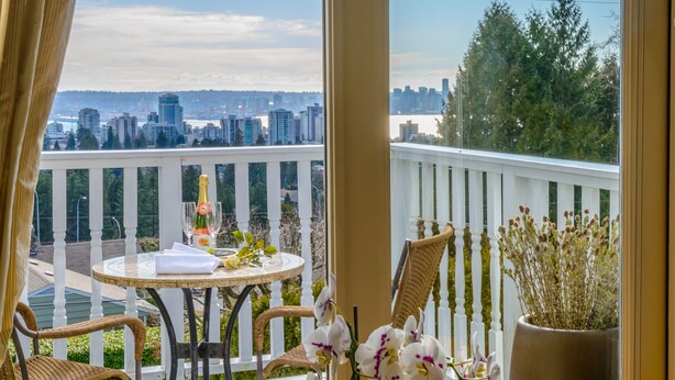 Un balcon avec une table dressée pour deux personnes, un pot de fleurs et une vue sur les toits de la ville.