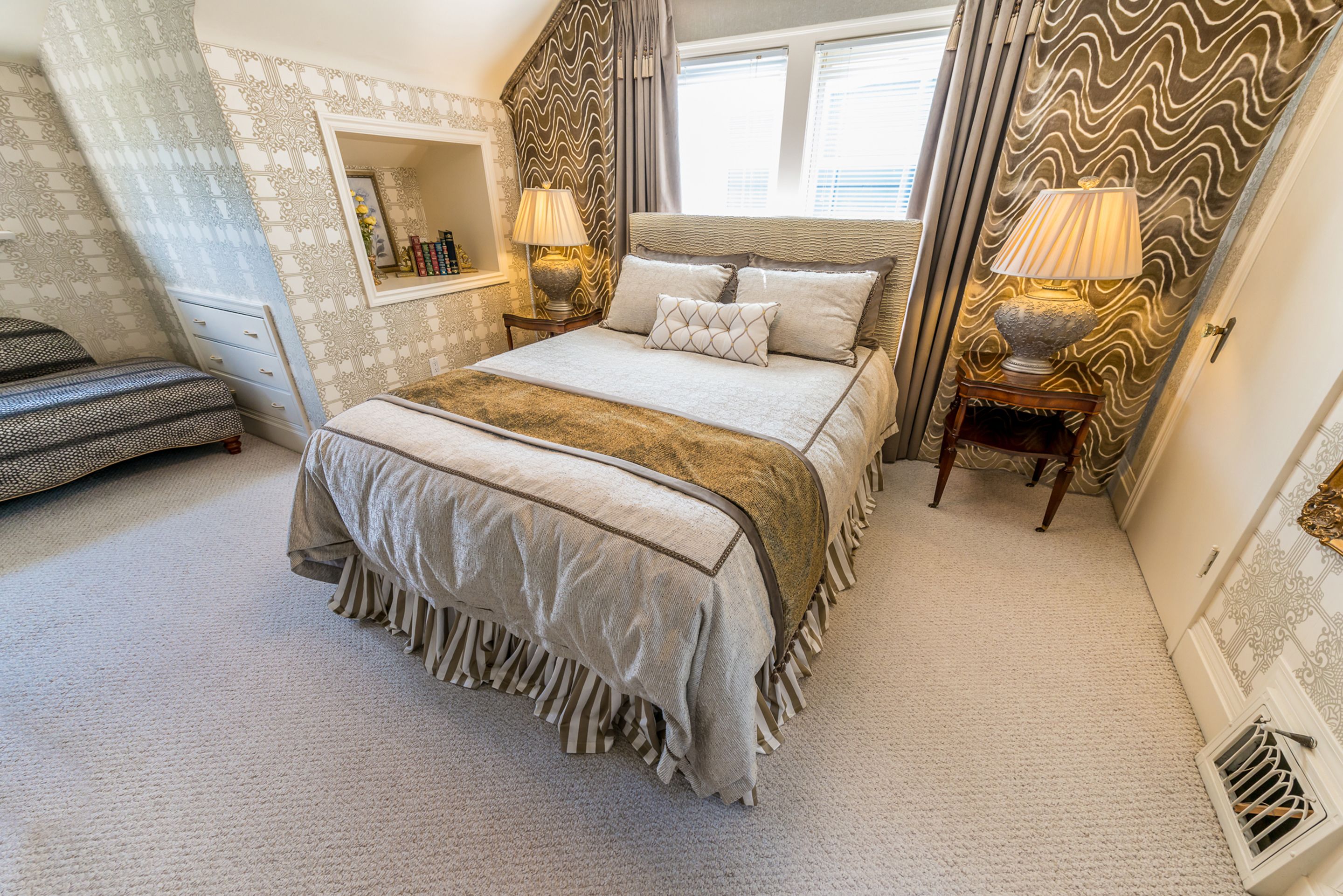 Une chambre à coucher avec un grand lit, deux tables de chevet avec des lampes, une commode, un miroir et une fenêtre avec des rideaux.