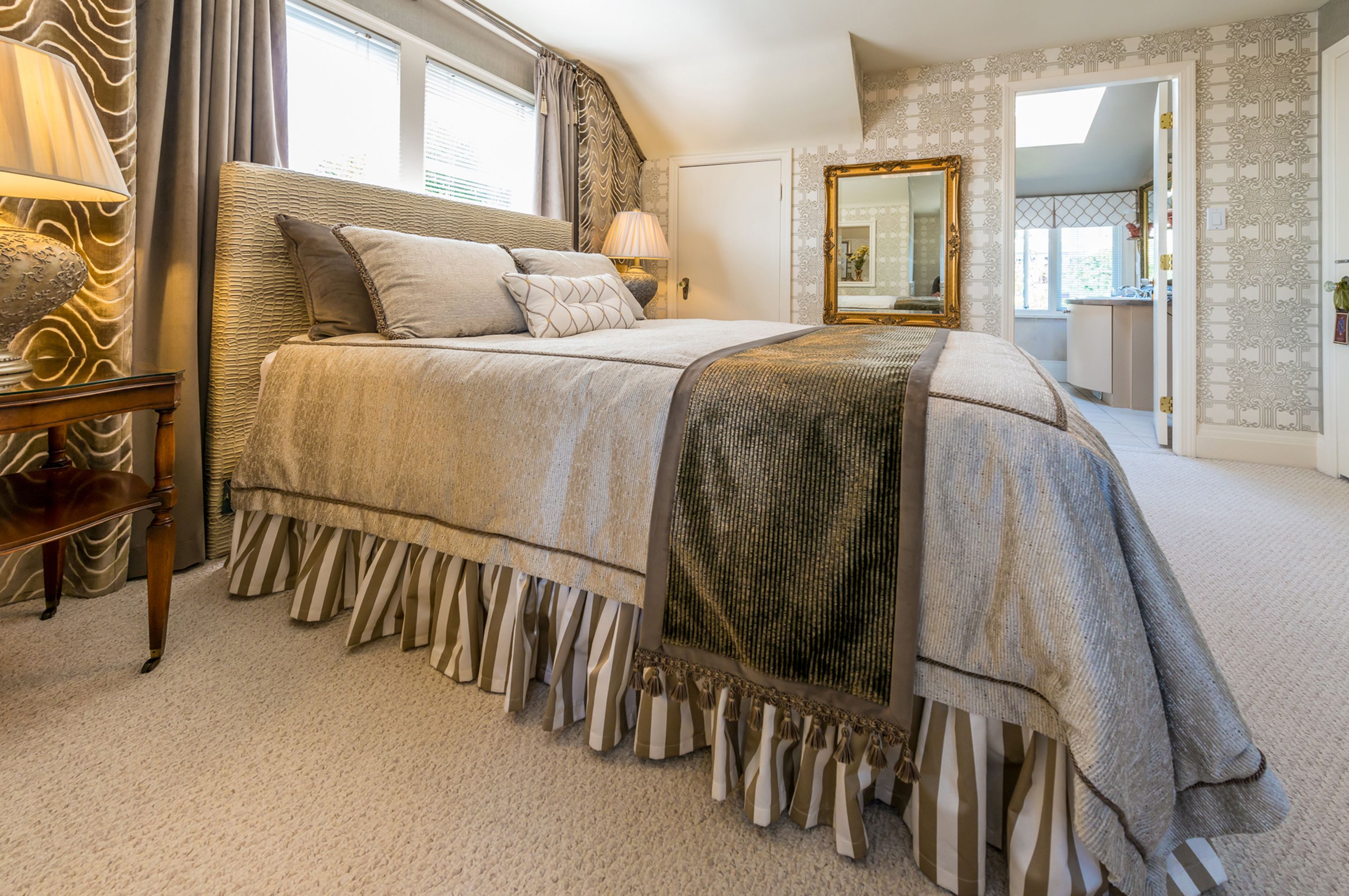 Een slaapkamer met een groot bed, een nachtkastje, een lamp, een spiegel en uitzicht op de badkamer.