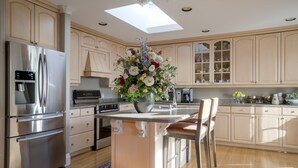 Une cuisine moderne dotée d’un îlot central, d’appareils électroménagers en acier inoxydable et de meubles de rangement en bois clair.