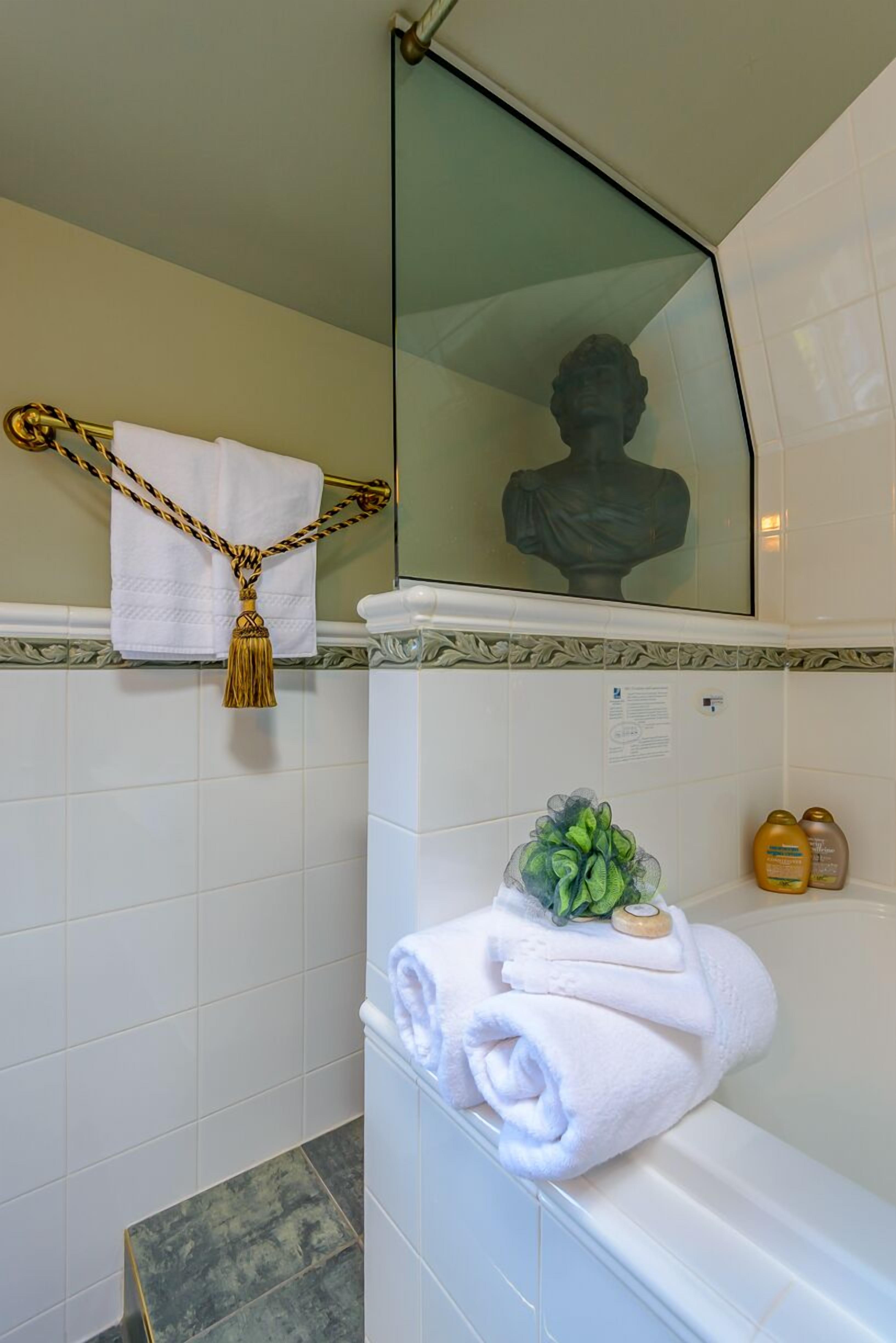 Une salle de bain carrelée de carreaux blancs, dotée d’une douche en verre, d’une baignoire blanche et d’un porte-serviettes orné d’une frange dorée.