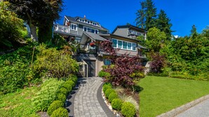 Une maison à deux étages, avec un chemin de pierre menant à la porte d’entrée, entourée d’une végétation luxuriante et d’une pelouse bien entretenue.