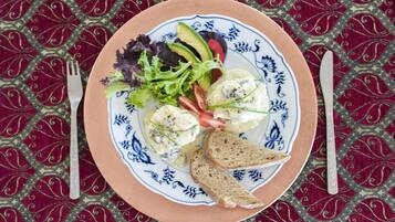 Un plato con ensalada, rebanadas de aguacate y pan sobre un mantel estampado.