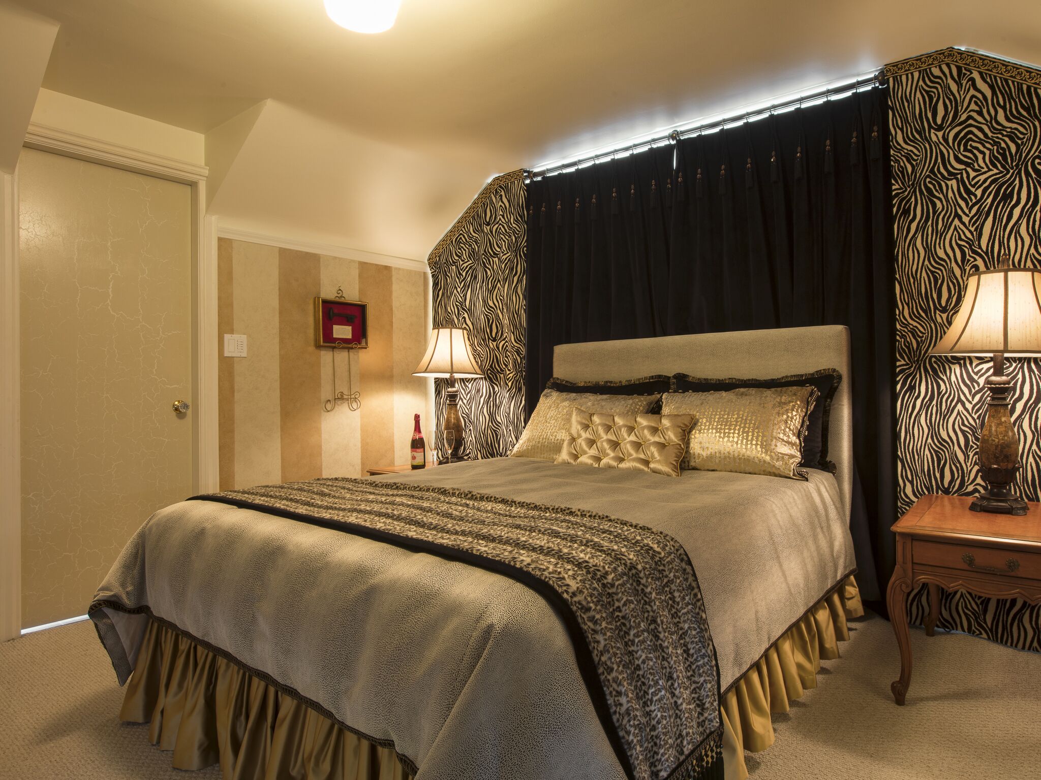 Een slaapkamer met een groot bed, gordijnen met een zebraprint en een nachtkastje met een lamp.