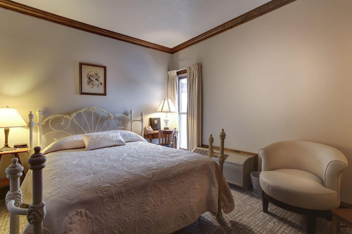 A neatly arranged bedroom with a bed, chair, bedside table, lamp, and a framed picture on the wall.
