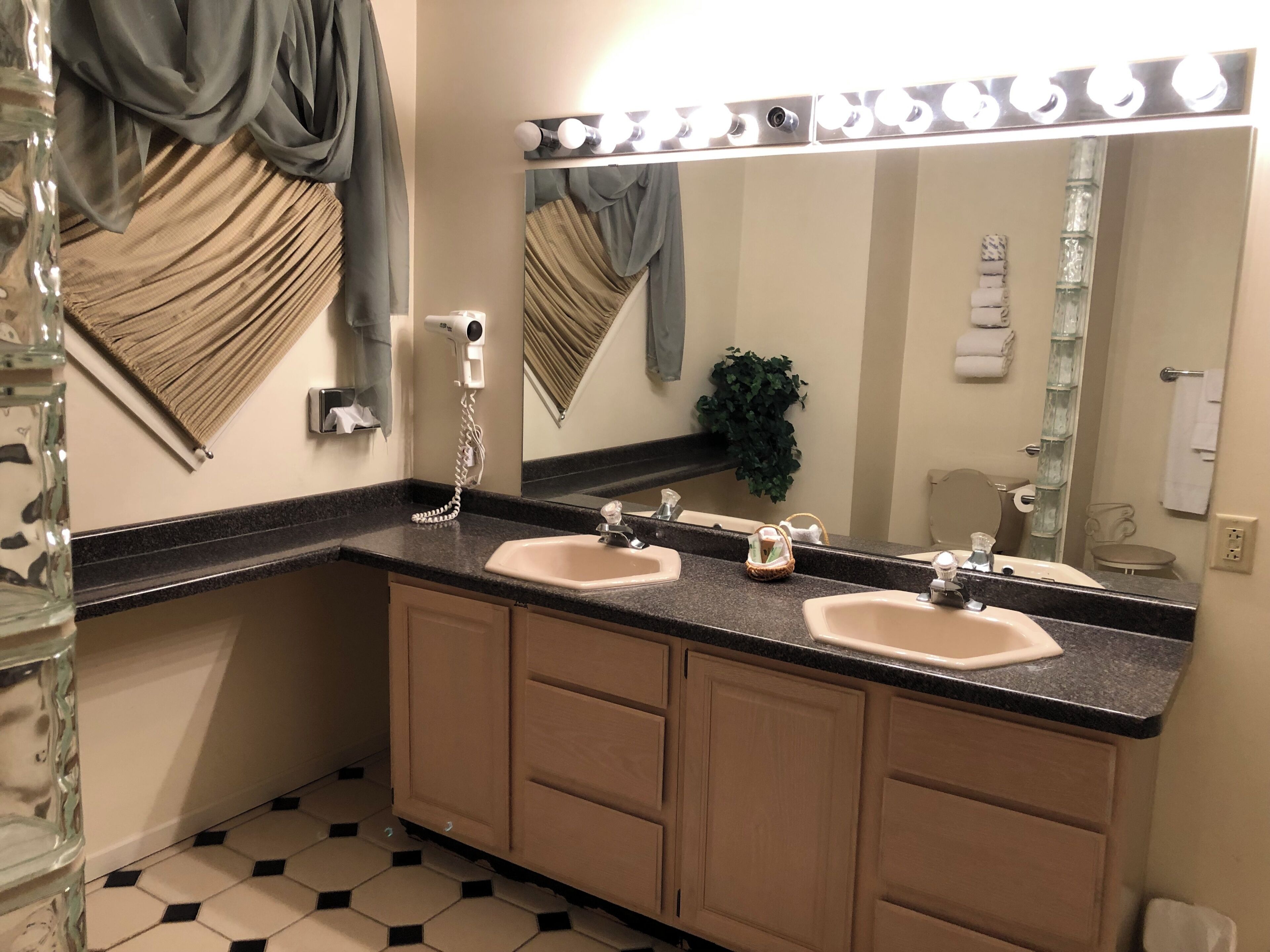 A bathroom with two sinks, a vanity mirror, a hairdryer, and a towel rack.