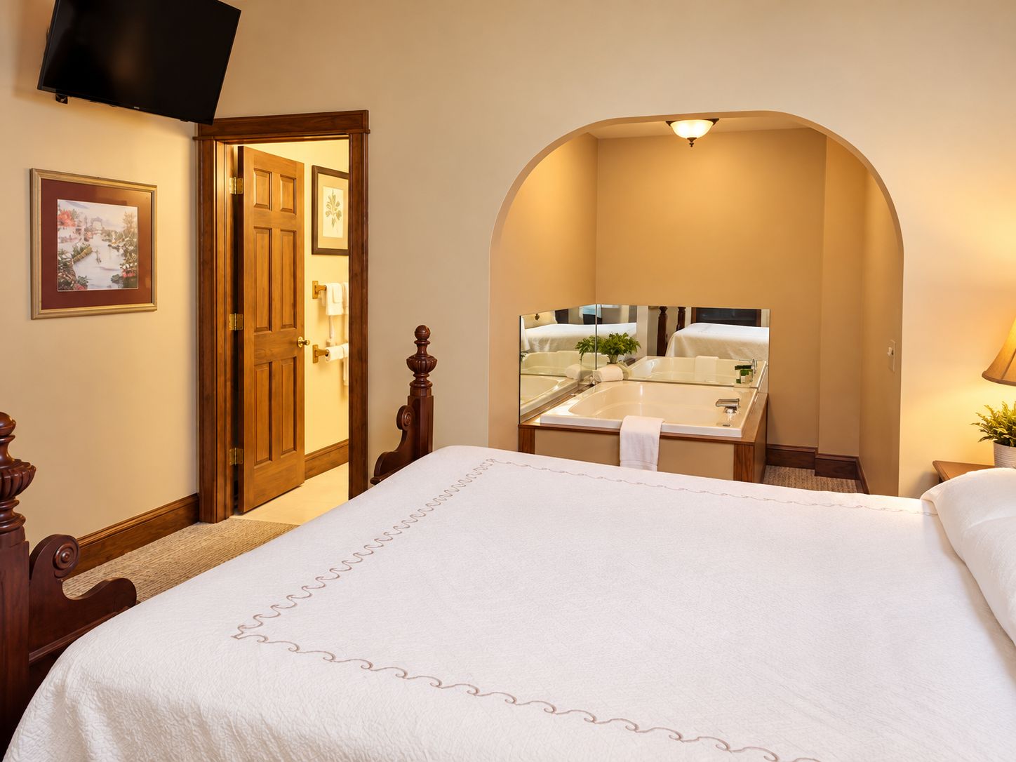 Una habitación de hotel con una cama grande, un baño con lavamanos y espejo, y una puerta que da a otra habitación.