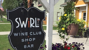 Edessä kukkapenkki ja sen yläpuolella kyltti, jossa lukee: «SWiRL WINE CLUB SHOP BAR».
