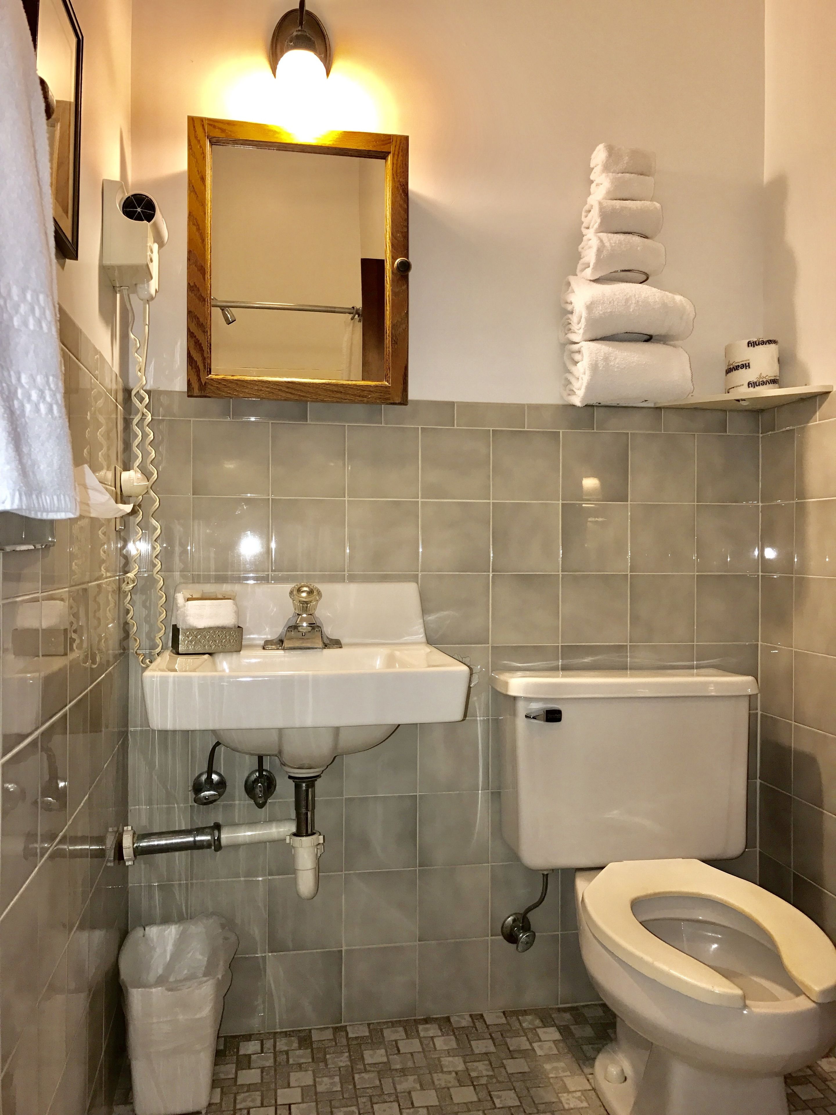 A bathroom with a sink, toilet, and mirror. There are towels and toilet paper on the wall.