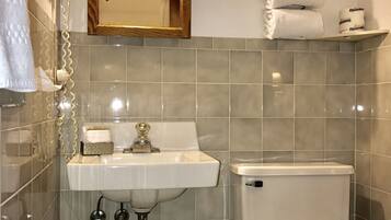 A bathroom with a sink, toilet, and mirror. There are towels and toilet paper on the wall.