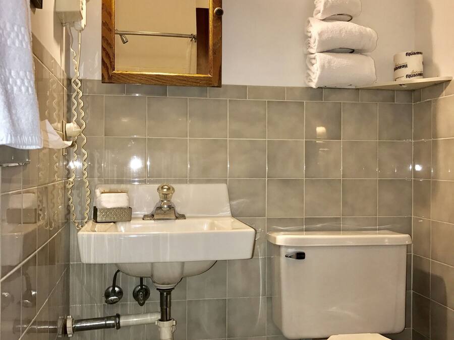 A bathroom with a sink, toilet, and mirror. There are towels and toilet paper on the wall.