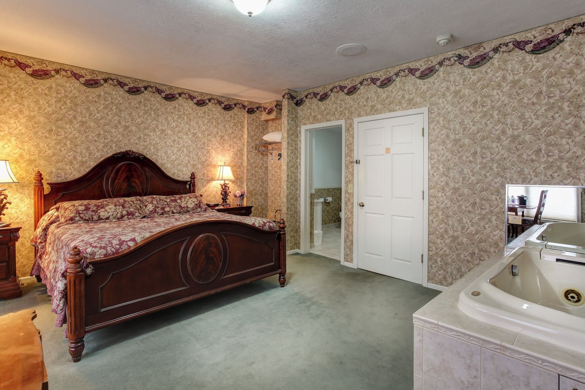 A bedroom with a large bed, a walk-in closet, and a bathroom with a bathtub.