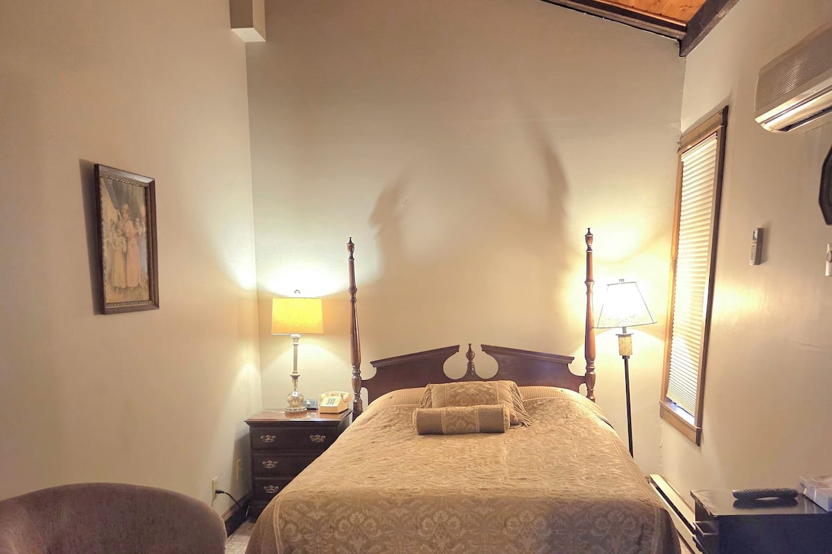 A bedroom with a bed, a chair, a desk, and a lamp.