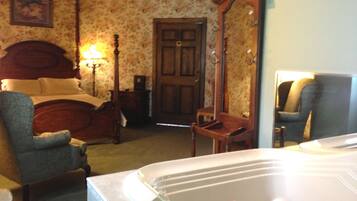 A bedroom with a bed, a chair, a wooden wardrobe, a mirror, and a bathtub.