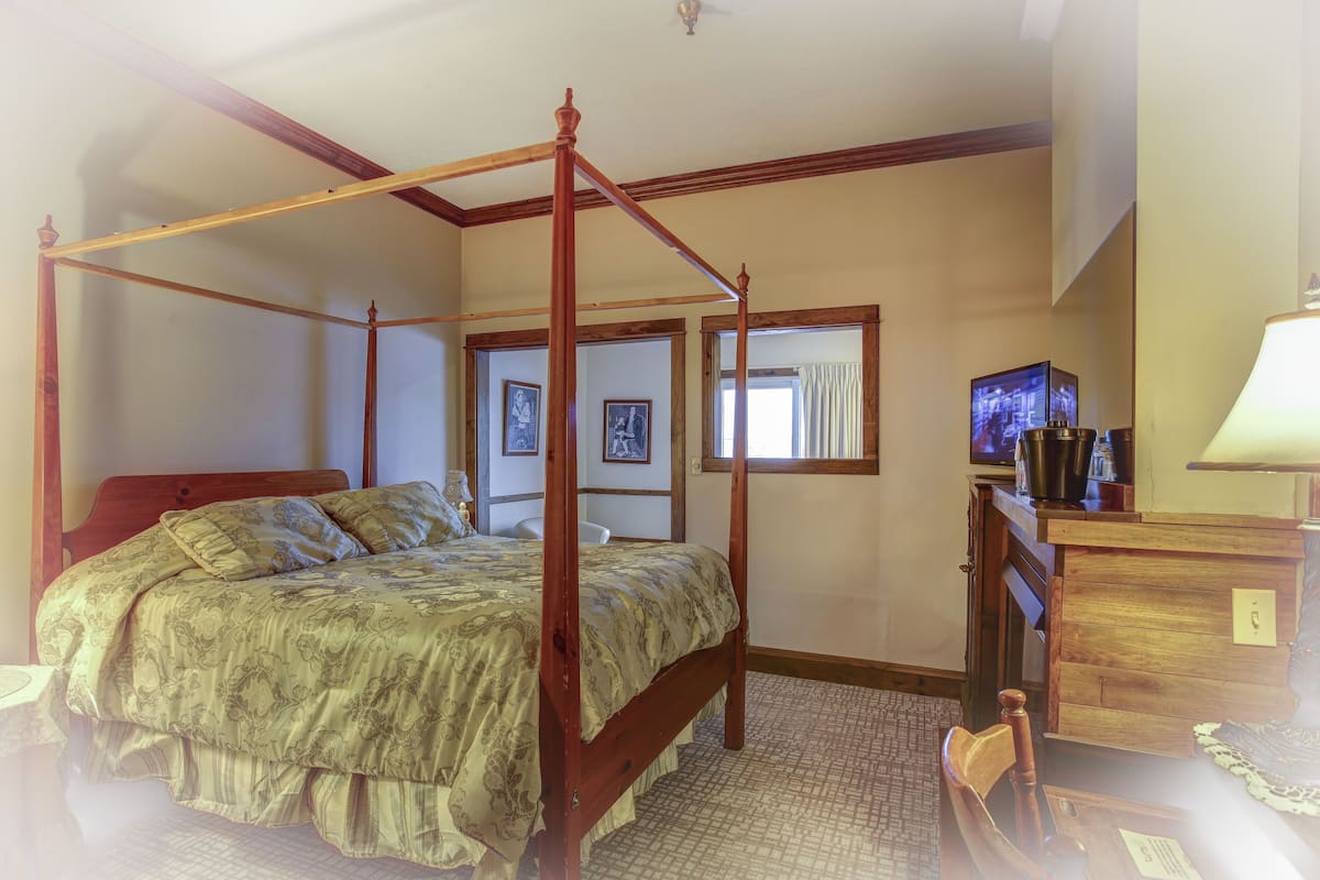 A four-poster bed with a wooden frame, a desk with a lamp, and a television on a wooden cabinet.