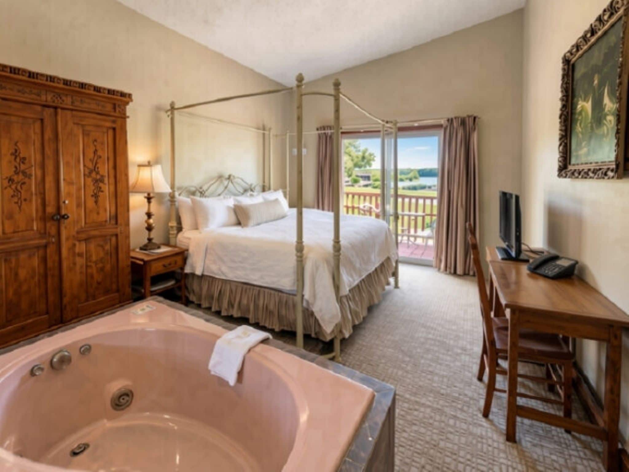 A bedroom with a four-poster bed, a large bathtub, a desk with a telephone, and a view of the outdoors.