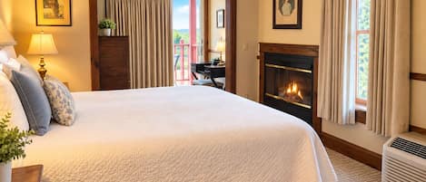A hotel room with a large bed, a fireplace, a desk with a lamp, and a view of the outdoors.