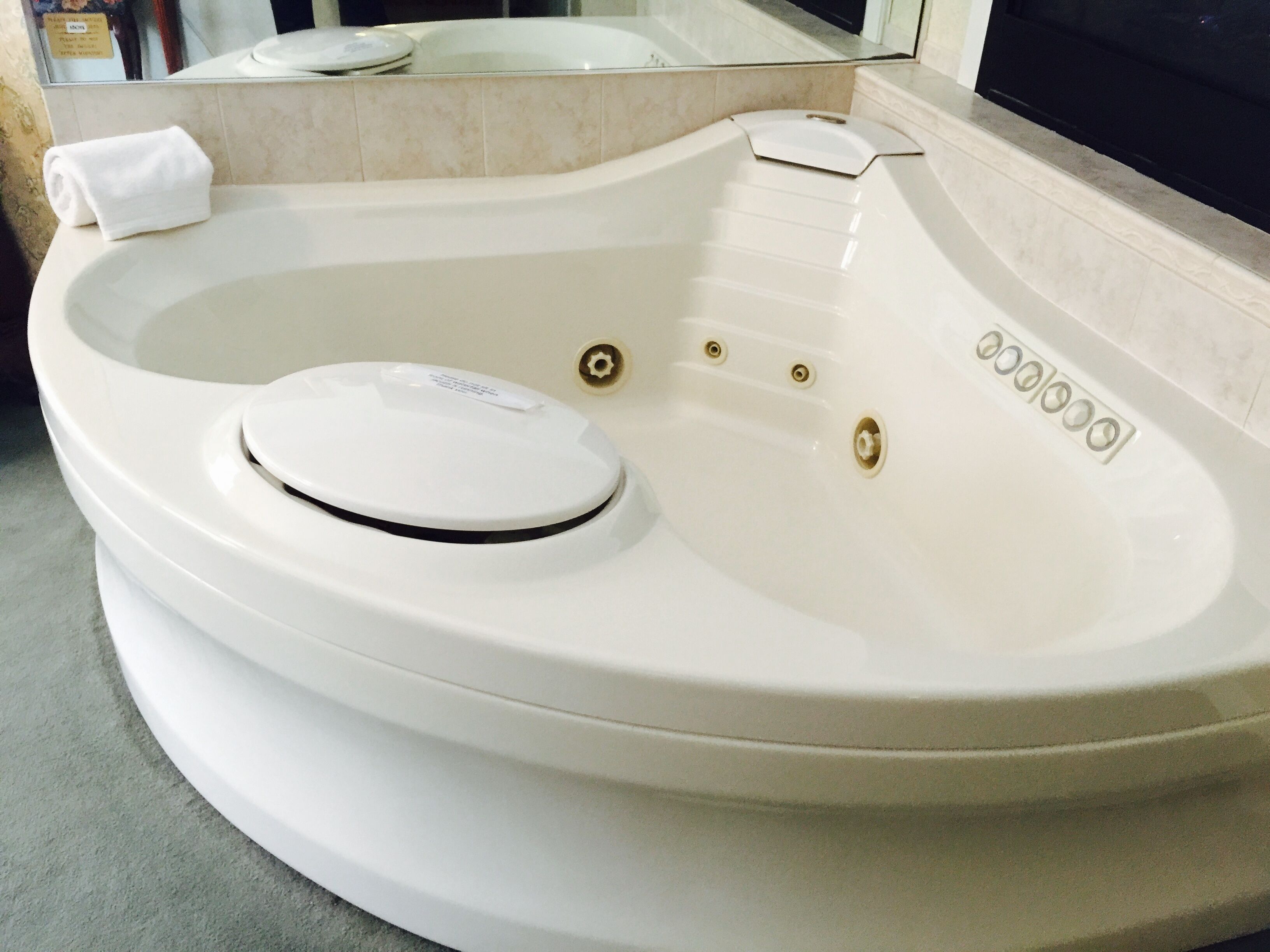 A white hot tub with a control panel, a towel, and a mirror reflecting the tub.