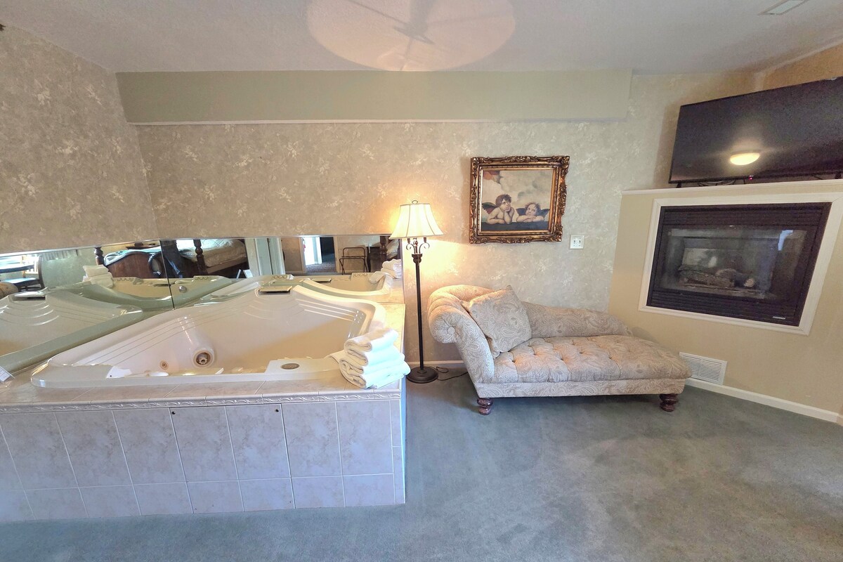 A room with a large bathtub, a sofa, a framed picture on the wall, and a fireplace.