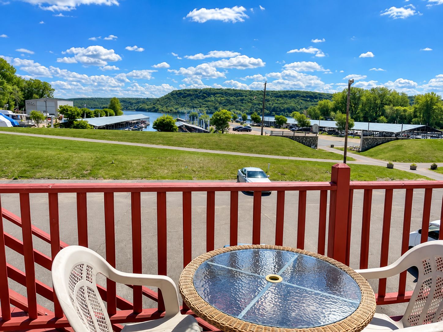 A balcony with a glass table and chairs, overlooking a scenic view of a lake and a small town.