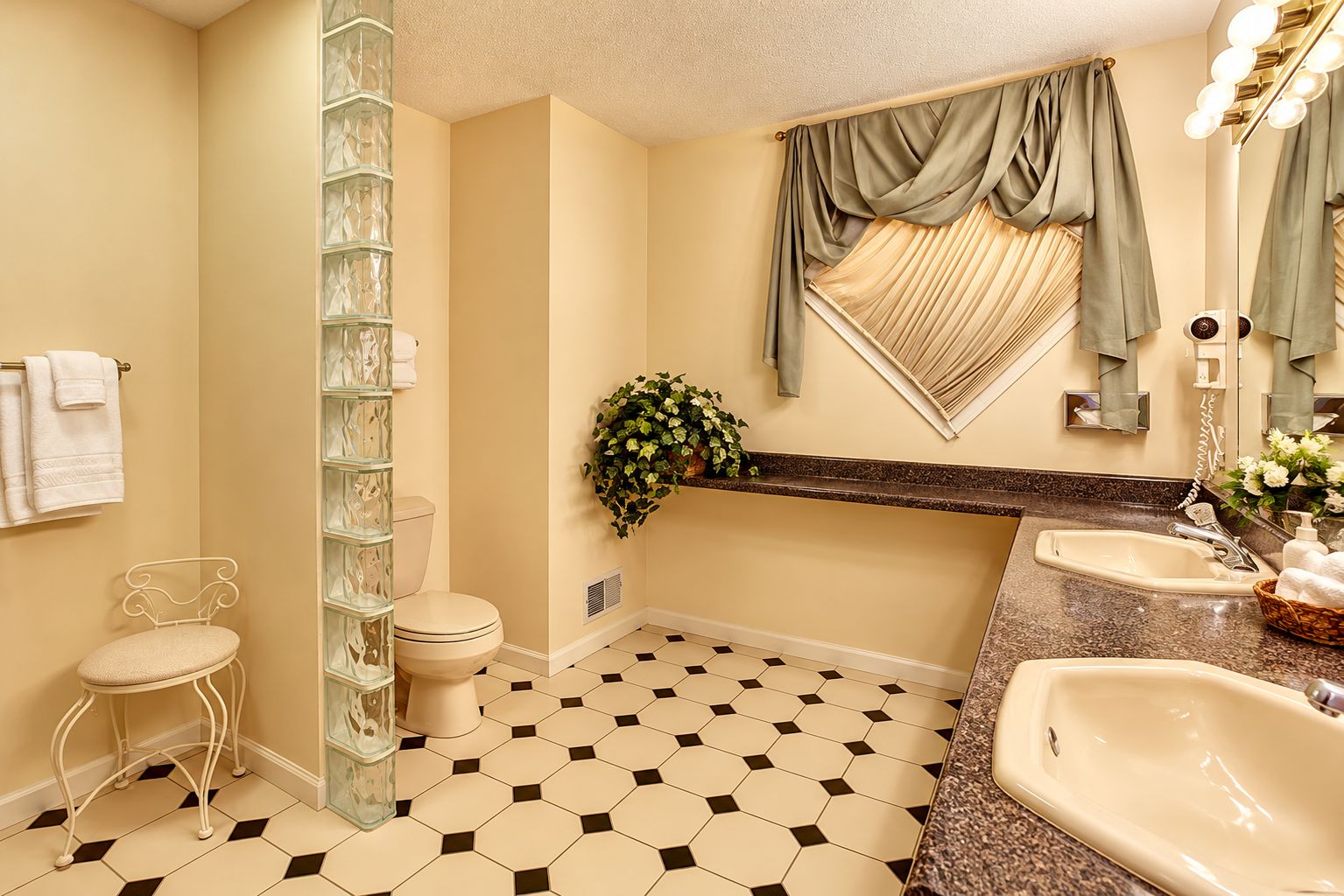 A bathroom with a toilet, sink, and vanity. There is a glass shower enclosure and a potted plant on the vanity.