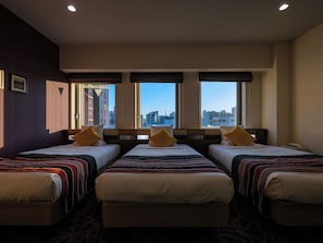 Habitación de hotel con tres camas, ventanas amplias y vistas a la ciudad.