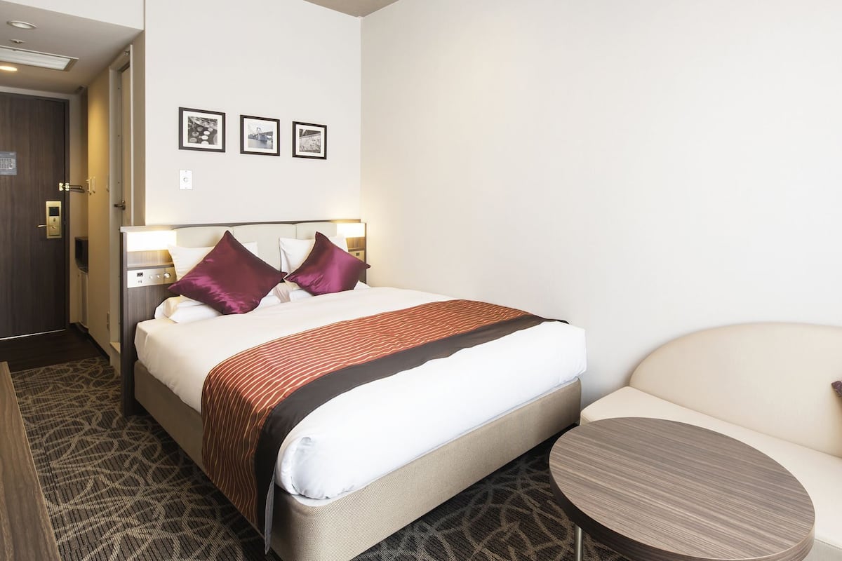 Une chambre d’hôtel avec un lit, un canapé, une petite table et trois tableaux encadrés accrochés au mur.