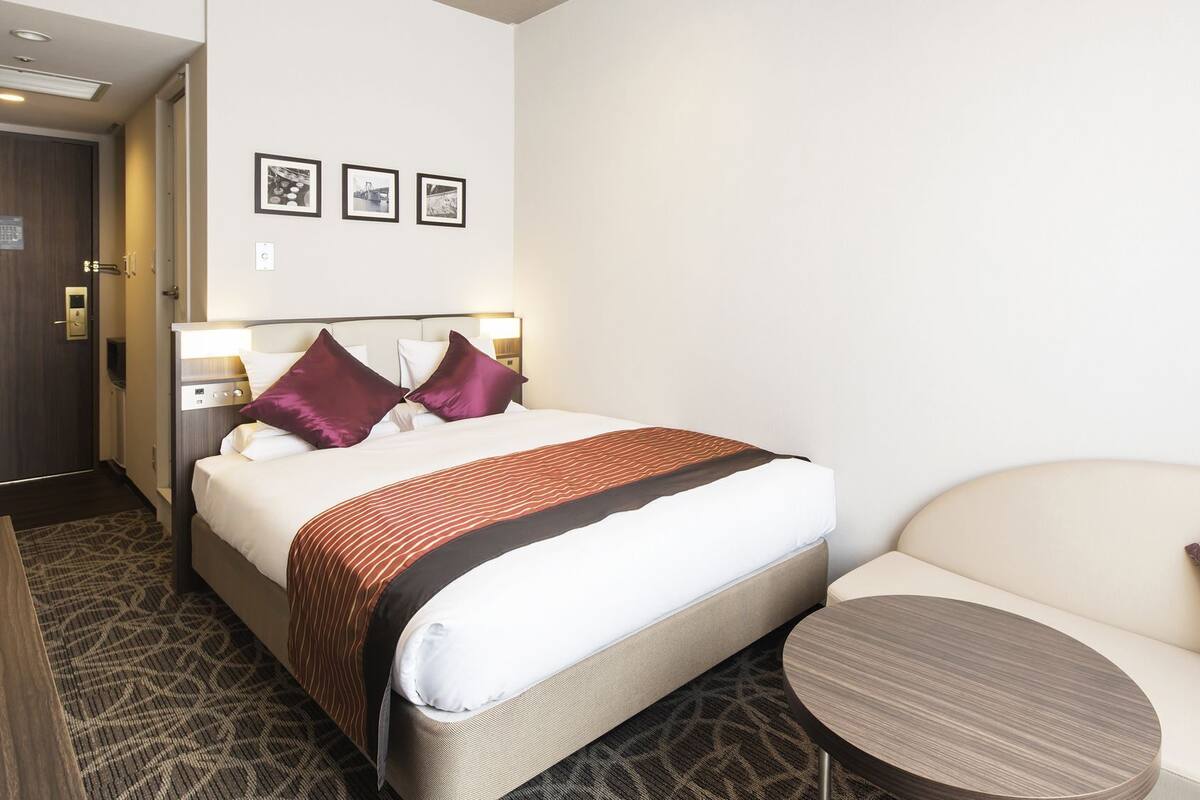 A hotel room with a bed, a sofa, a small table, and three framed pictures on the wall.