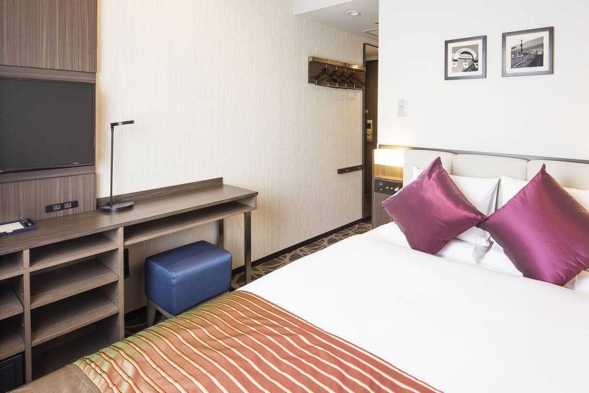 Une chambre d’hôtel avec un lit, un bureau, une télévision et deux tableaux encadrés au mur.
