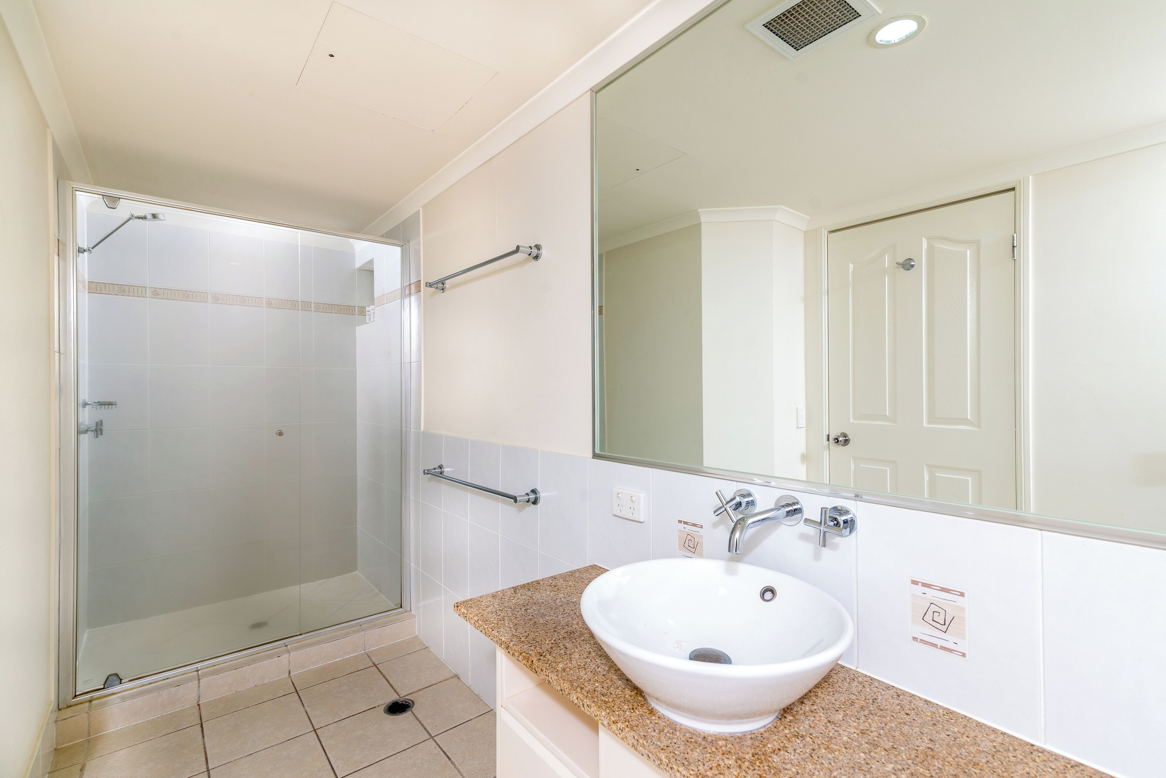 Une salle de bain avec une douche à parois de verre, un lavabo blanc et un grand miroir.