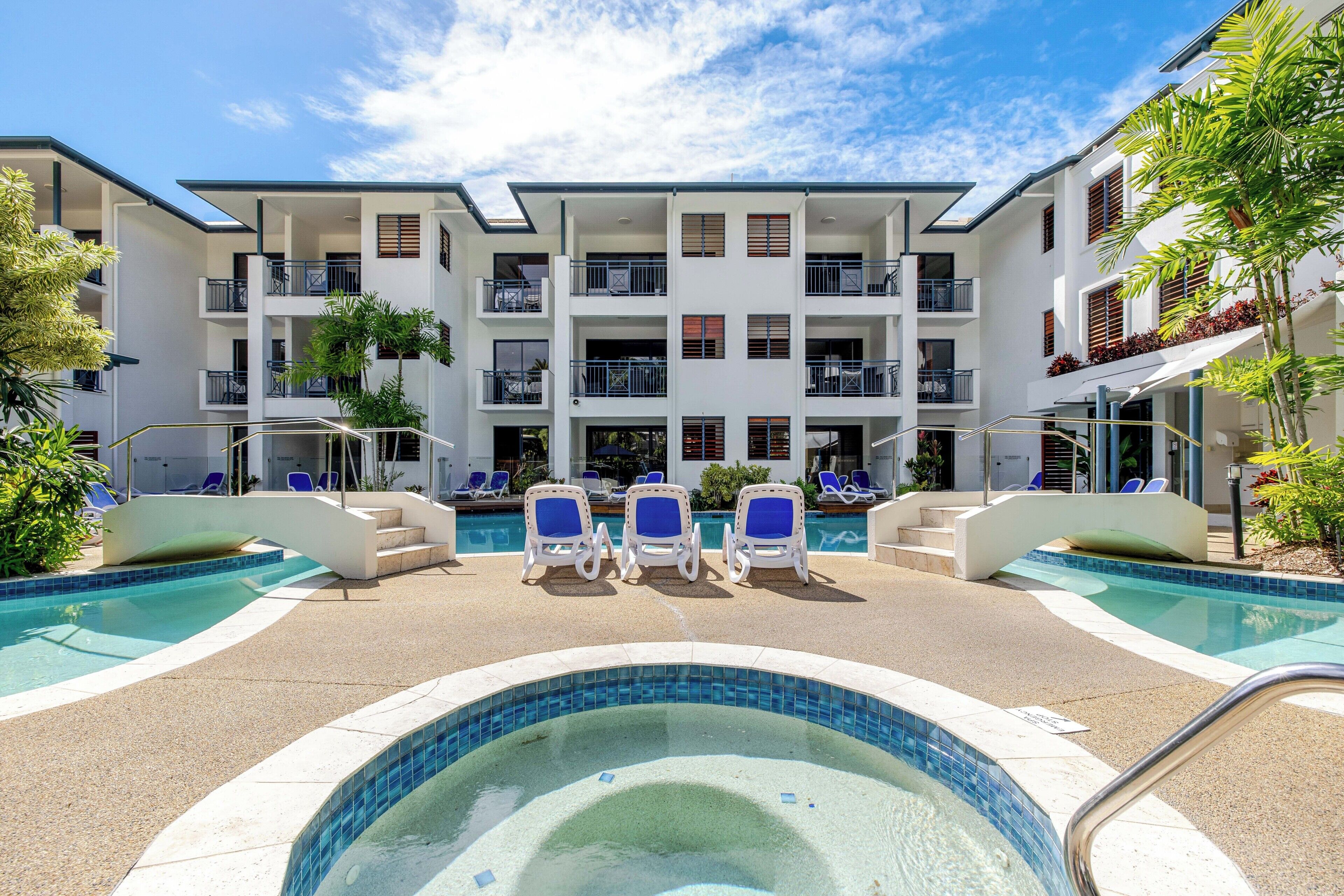 Un hôtel doté d’une piscine, de chaises longues et d’un immeuble à plusieurs étages avec des balcons.