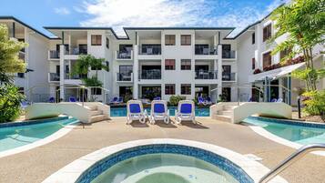A hotel with a swimming pool, lounge chairs, and a multi-story building with balconies.