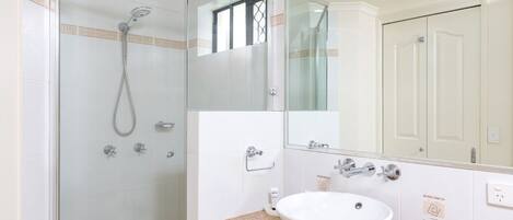 A bathroom with a glass-enclosed shower, a white sink, and a large mirror.