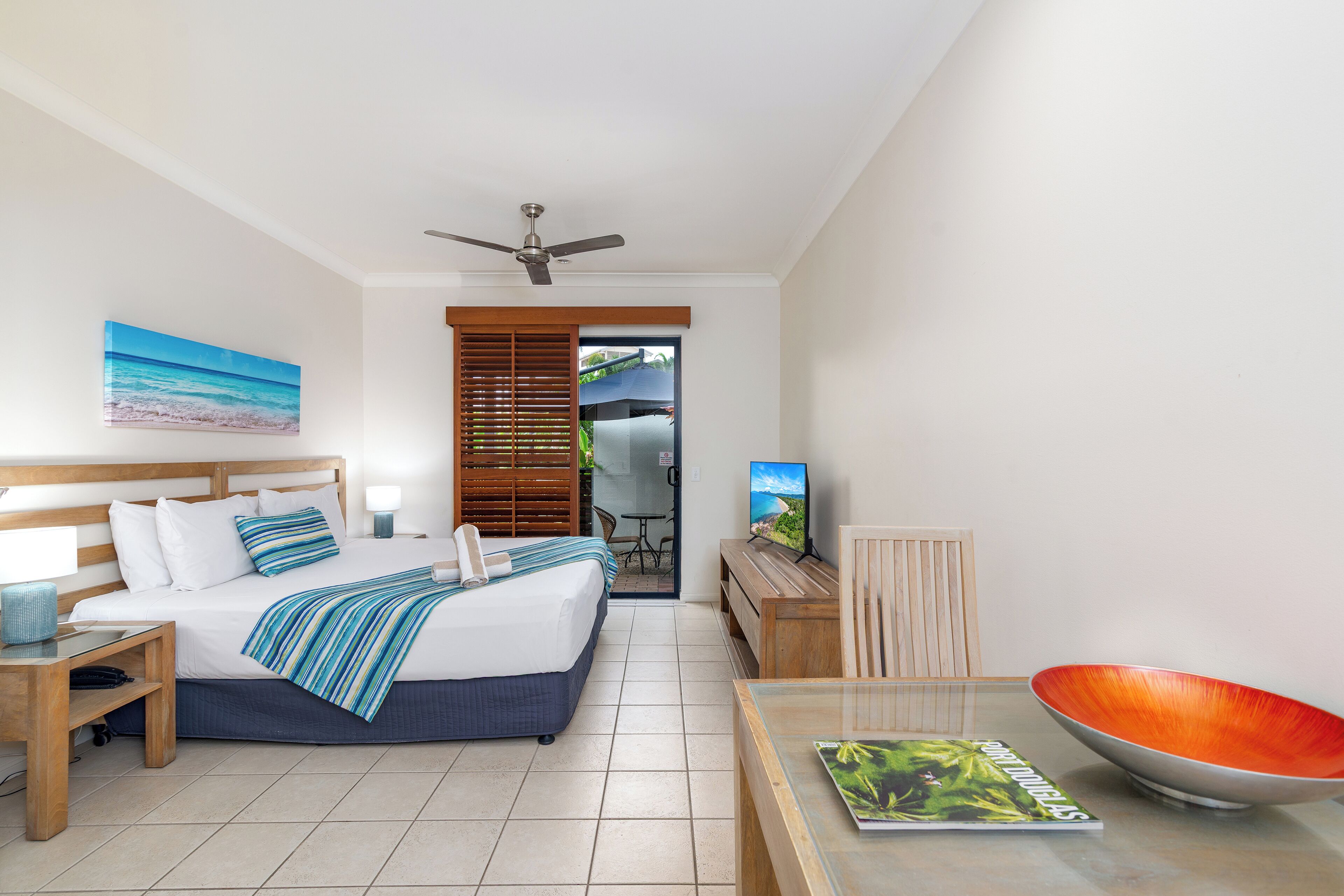 A hotel room with a bed, a television, a dining table, a bowl, and a painting.