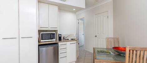 A compact kitchen with white cabinets, a stainless steel refrigerator, a microwave, and a coffee maker.