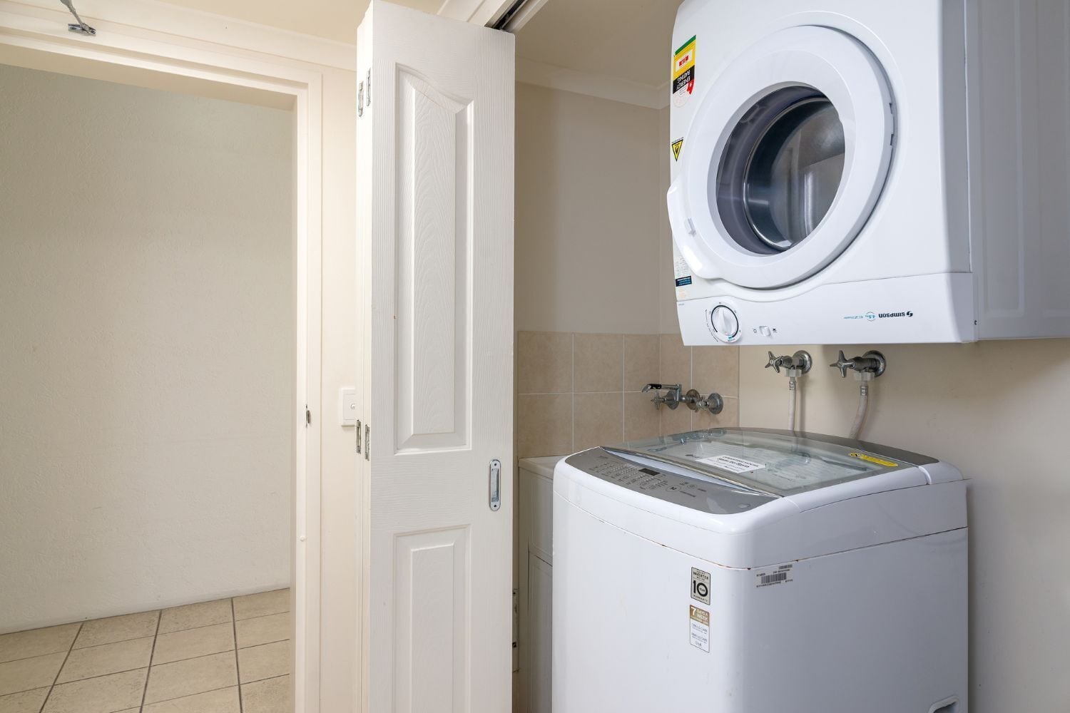 A laundry room with a front-loading washing machine and a dryer, a door, and tiled walls.