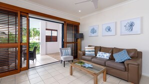 A modern living room with a brown leather sofa, a grey armchair, and a coffee table. There are three framed artworks on the wall and a ceiling fan. - Meridian Port Douglas - Adults only (Port Douglas)