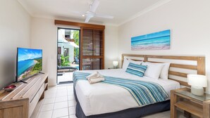 A hotel room with a bed, a TV, a ceiling fan, a painting, and a view of the outdoors. - Meridian Port Douglas - Adults only (Port Douglas)