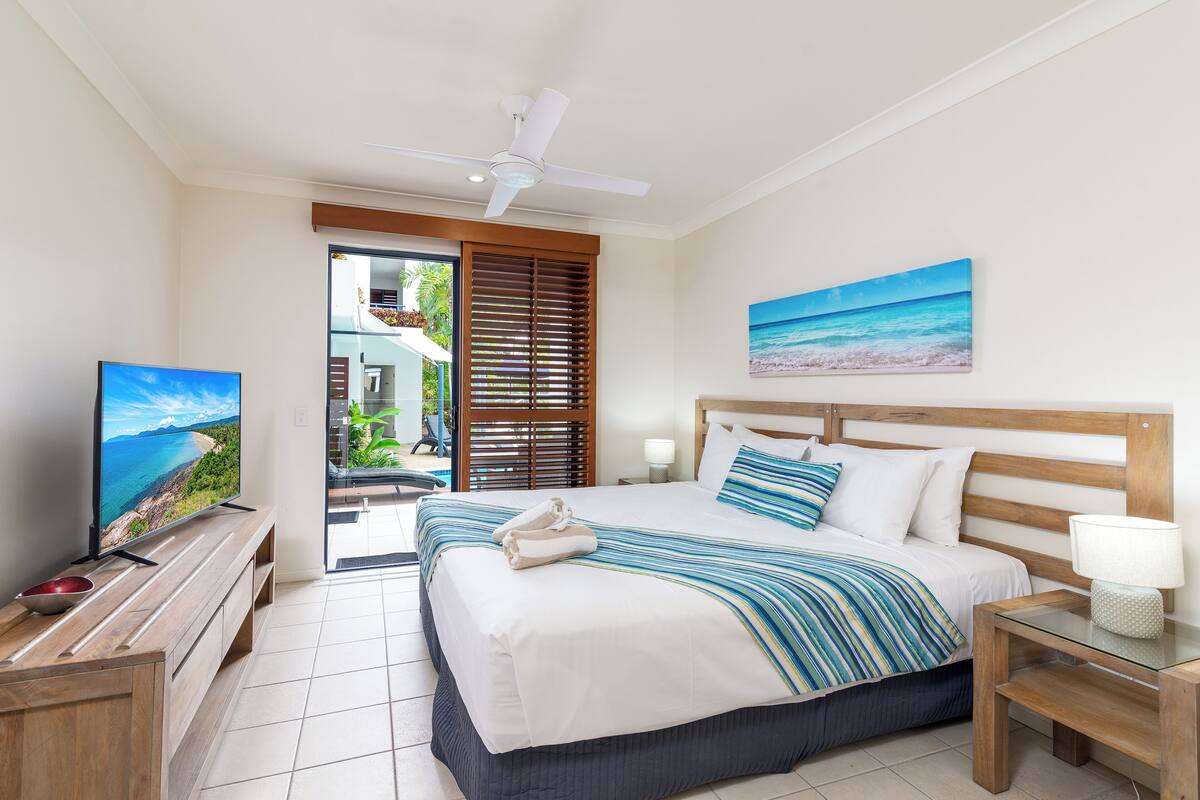 Ein Hotelzimmer mit Bett, Fernseher, Deckenventilator, einem Gemälde und Blick ins Freie.