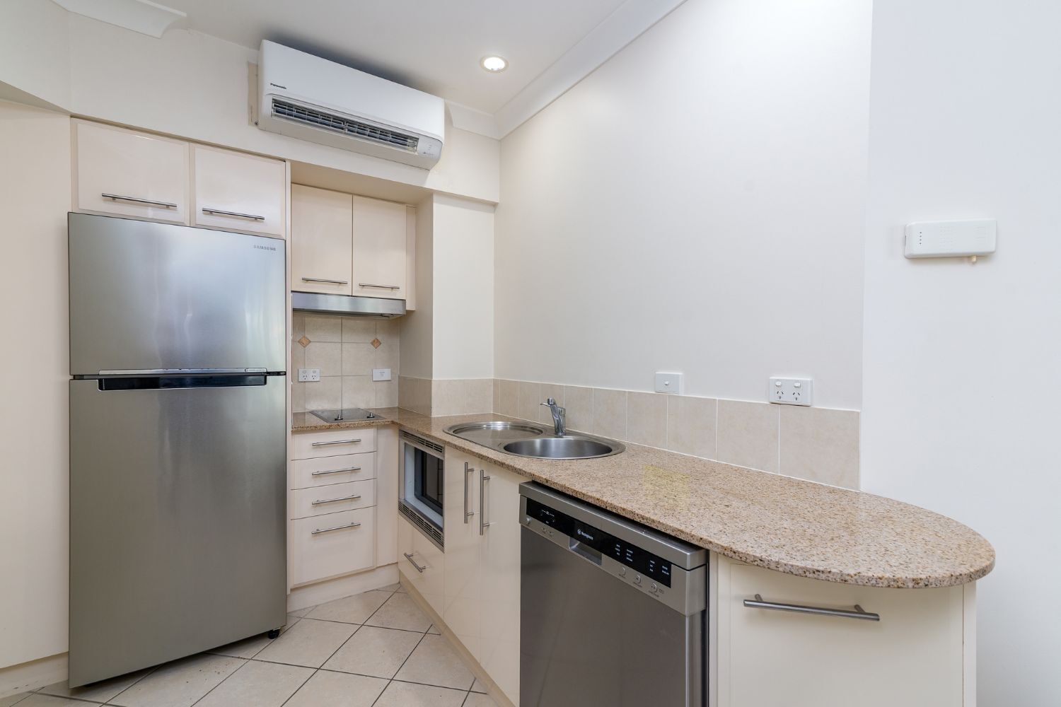 A compact kitchen with a stainless steel refrigerator, a dishwasher, a sink, and a built-in oven.