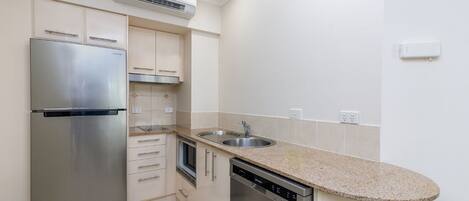 A compact kitchen with a stainless steel refrigerator, a dishwasher, a sink, and a built-in oven.