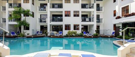 A modern hotel with a swimming pool, multiple balconies, and sun loungers.