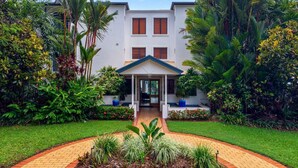A two-story building with a covered entrance, surrounded by lush greenery and a brick pathway. - Meridian Port Douglas - Adults only (Port Douglas)